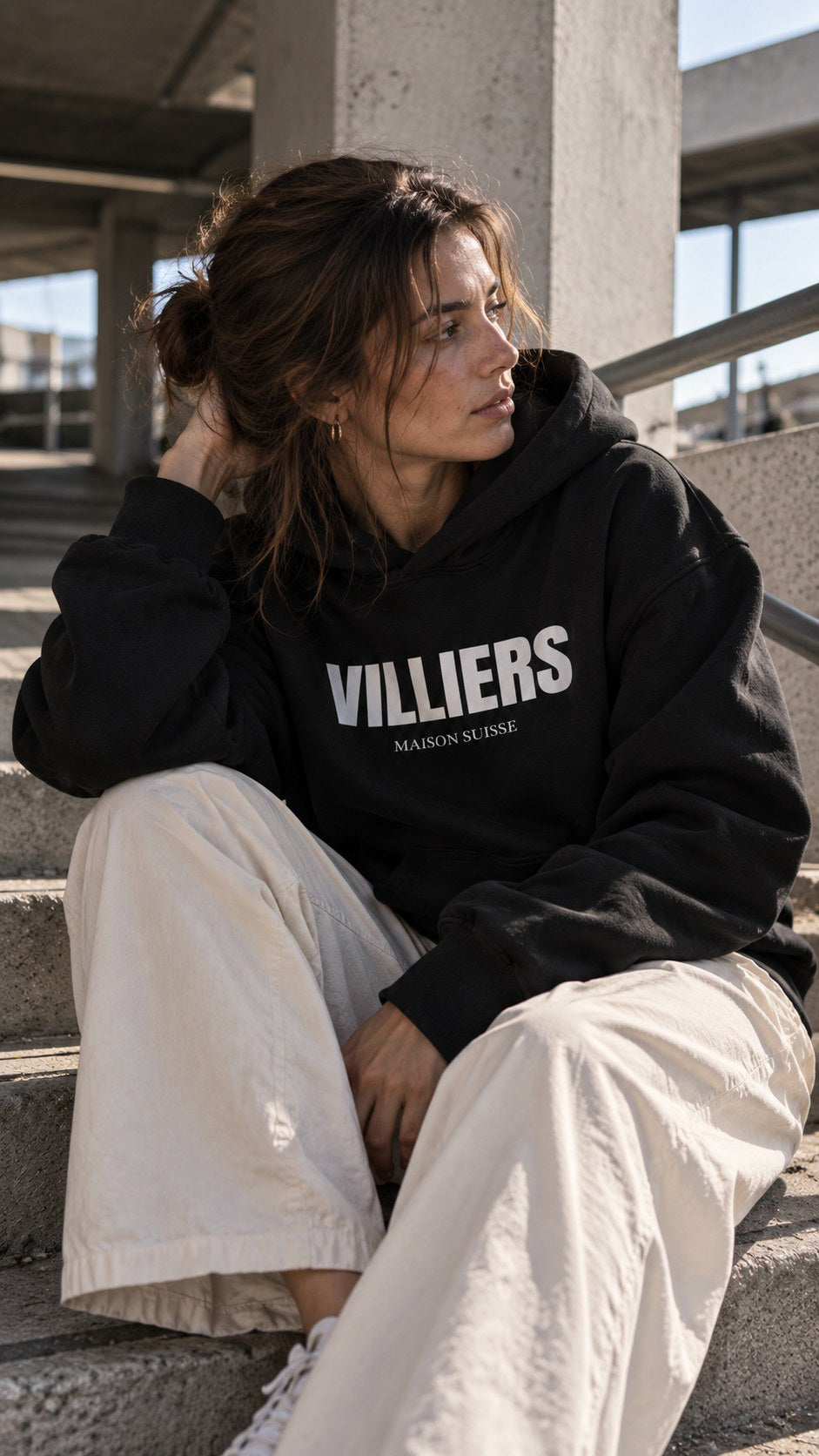Frau im schwarzen Villiers Hoodie sitzt auf einer Betontreppe