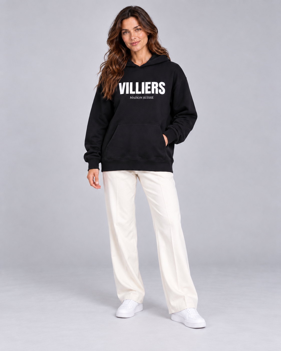 Frau trägt schwarzen Oversize Hoodie von Villiers Maison Suisse zu cremefarbener Hose, Ganzkörper von vorne
