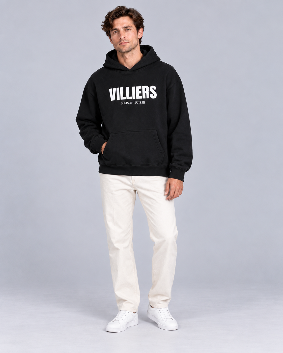 Mann trägt schwarzen Oversize Hoodie von Villiers Maison Suisse zu cremefarbener Hose, Ganzkörper von vorne