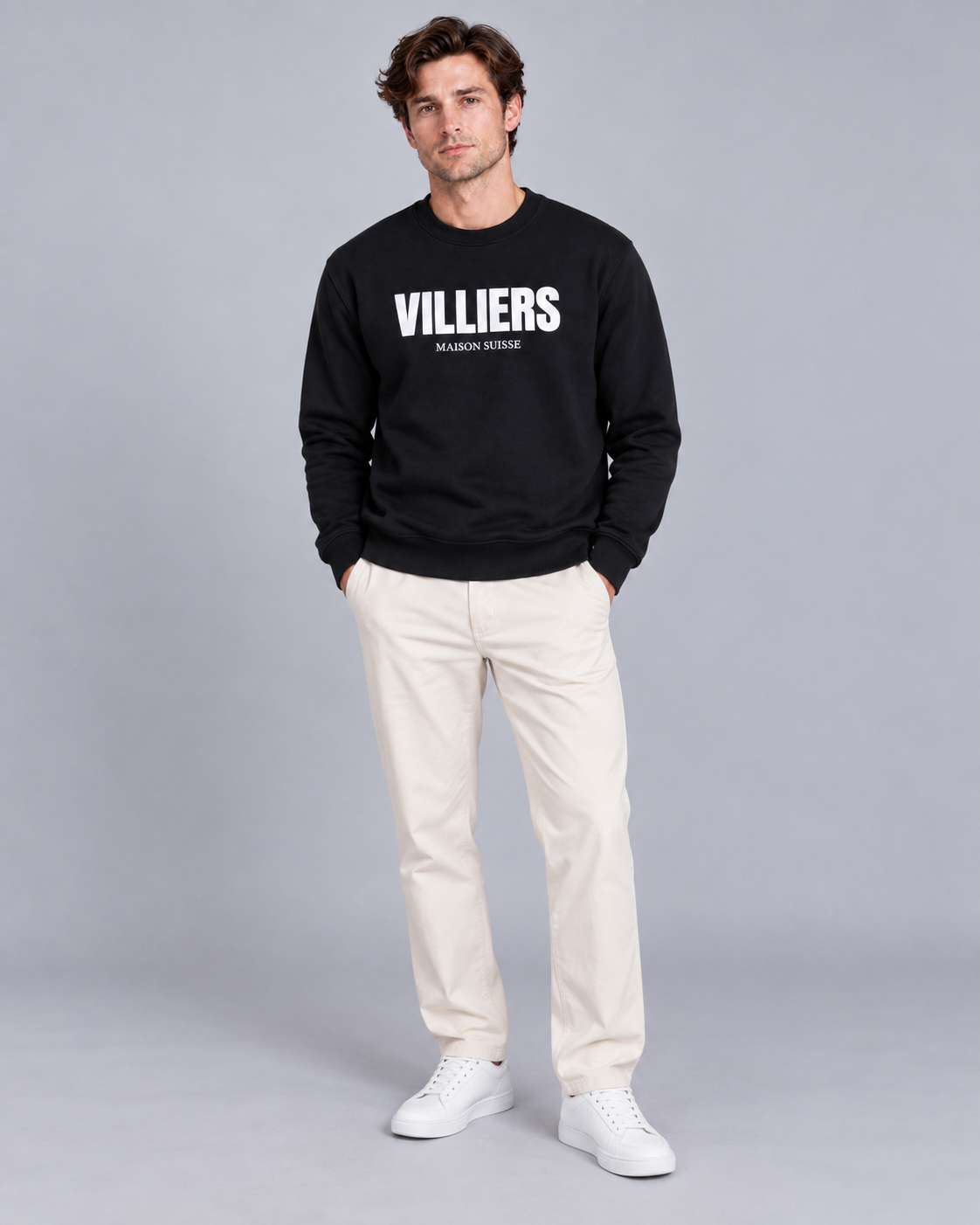 Mann trägt schwarzes Sweatshirt von Villiers Maison Suisse zu cremefarbener Hose, Ganzkörper von vorne
