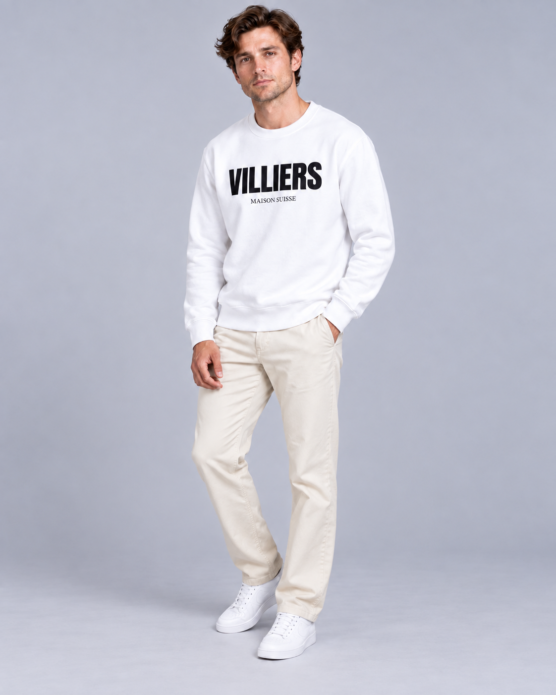 Mann trägt weisses Sweatshirt von Villiers Maison Suisse zu cremefarbener Hose, Ganzkörper von vorne
