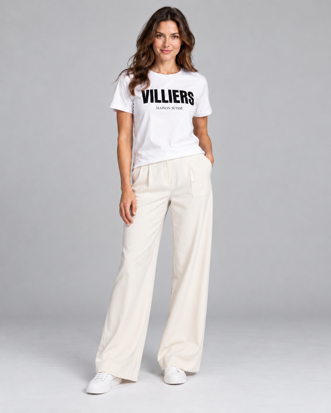 Frau trägt weisses T-Shirt von Villiers Maison Suisse zu cremefarbener Hose, Ganzkörper von vorne
