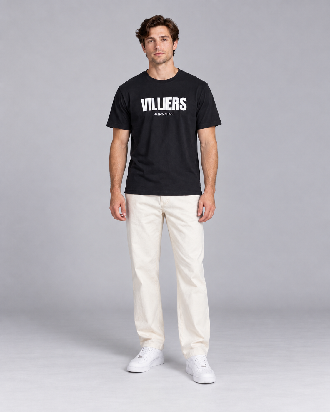 Mann trägt schwarzes T-Shirt von Villiers Maison Suisse zu cremefarbener Hose, Ganzkörper von vorne
