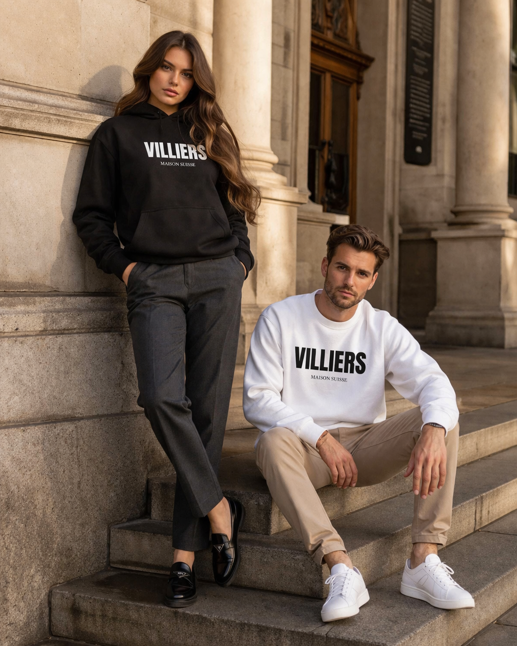 Frau mit schwarzem Hoodie und Mann mit weißem Sweatshirt von Villiers Maison Suisse auf einer Steintreppe
